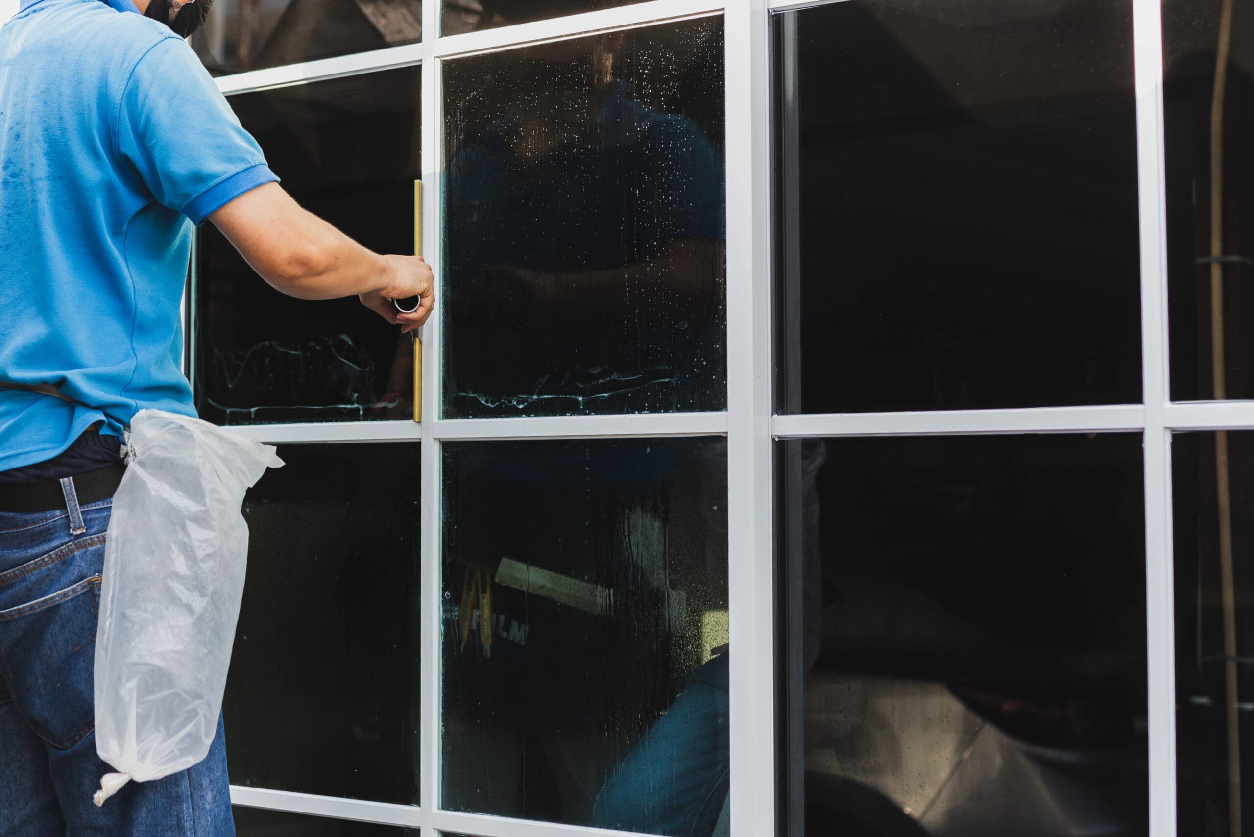 Worker use scraper cleaning window before installing tinting film